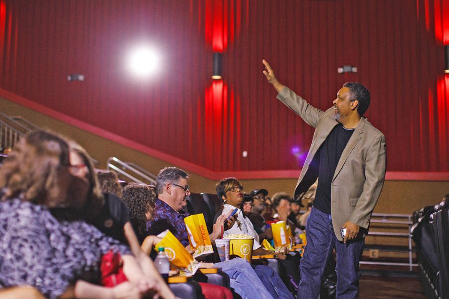 Willmott gestures to audience members seated in theatre auditorium.