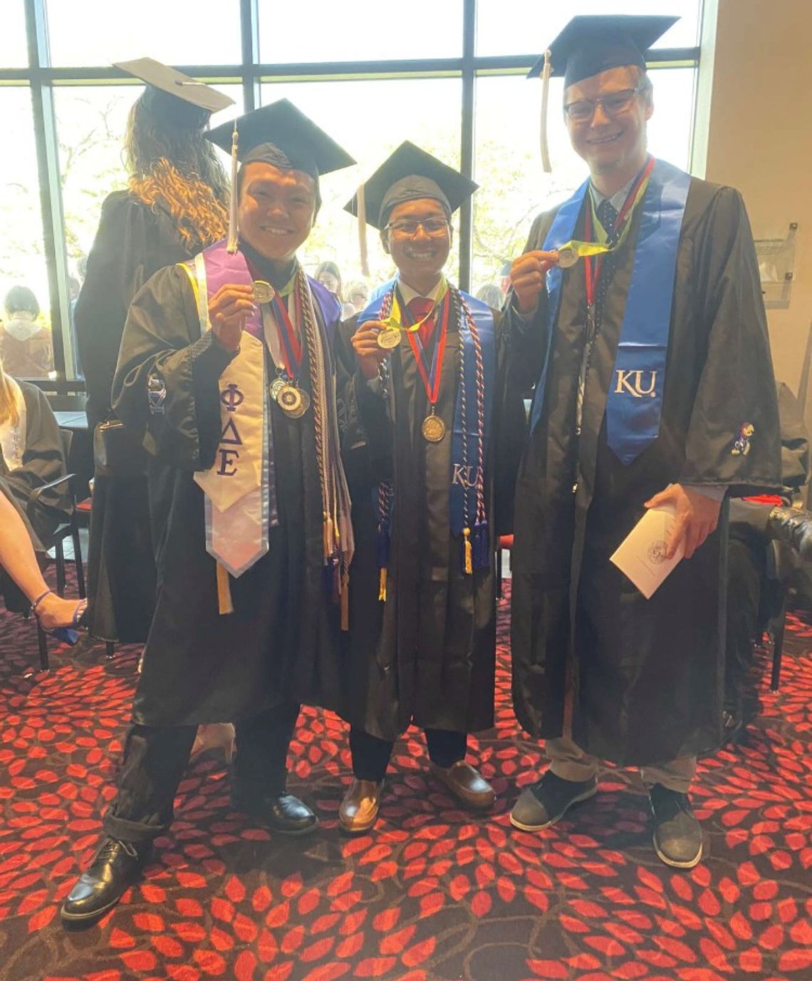 three people wearing graduation regalia holding their K-INBRE medals