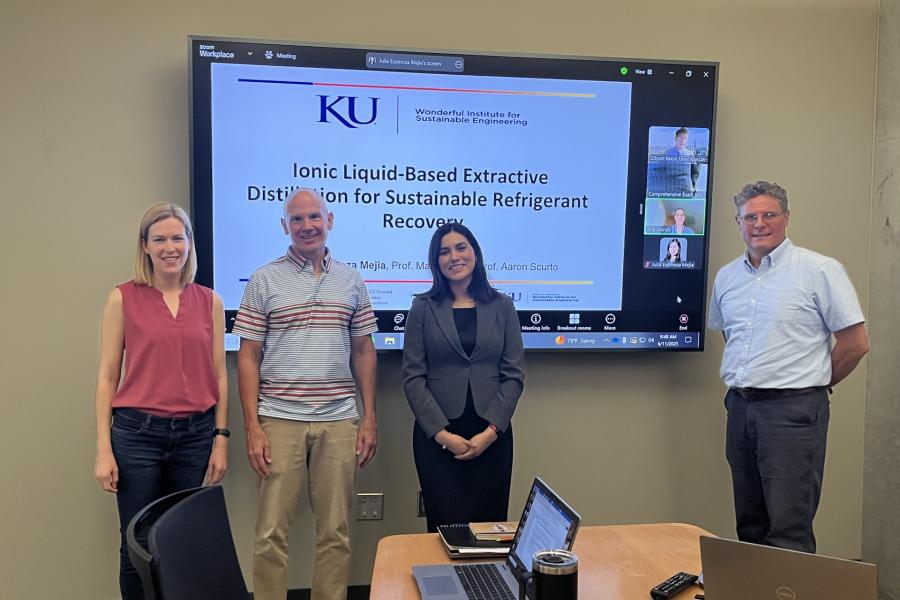 Four people standing in front of a screen smiling