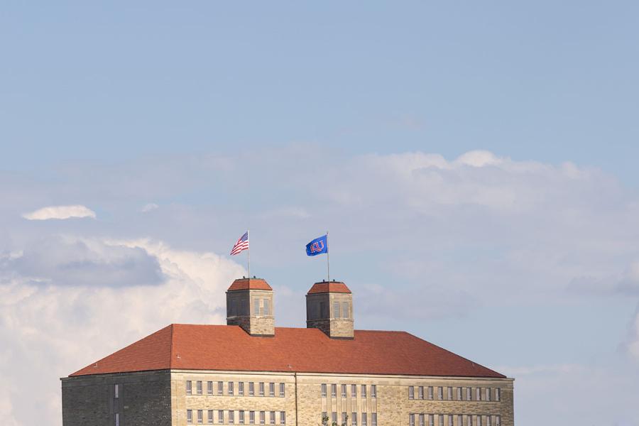Roof of Fraser Hall with KU, U.S. flags on cloudy day