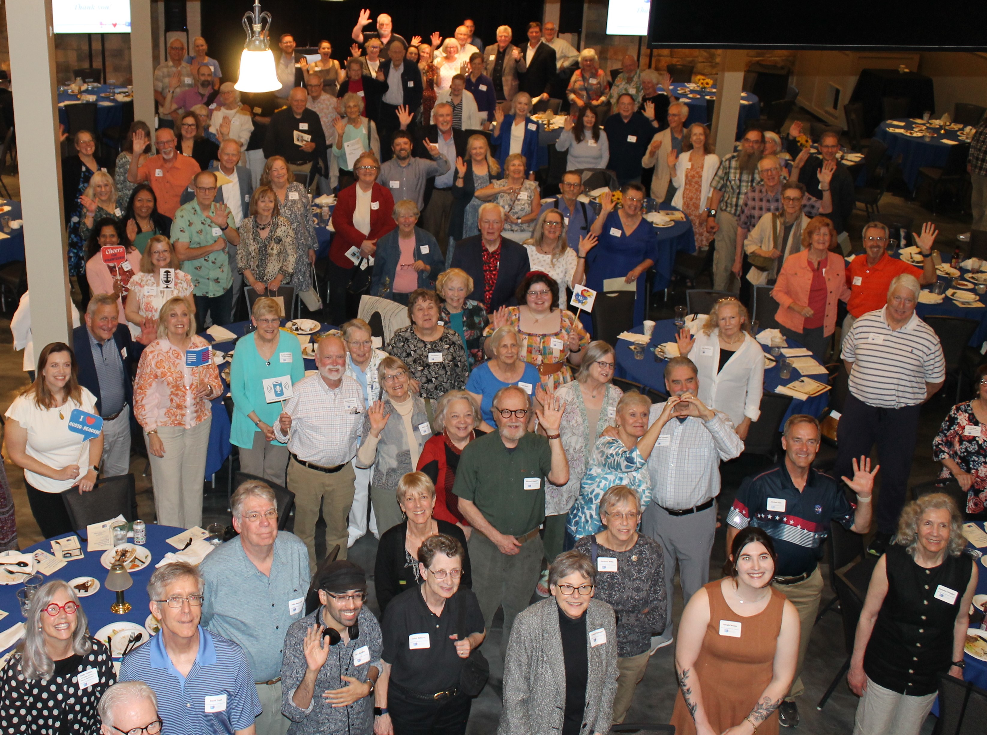 Over one hundred volunteers stand together smiling at Maceli's and looking up at the camera.
