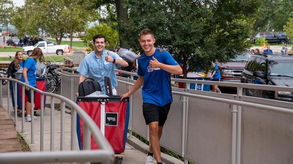 Students moving carts along sidewalk showing thumbs-up