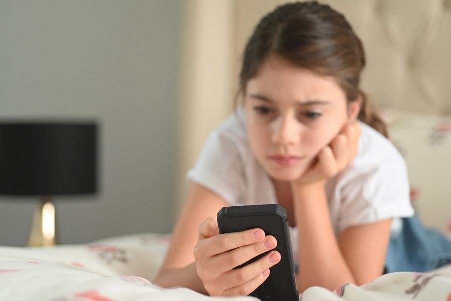 Young woman laying on bed looking at smartphone.