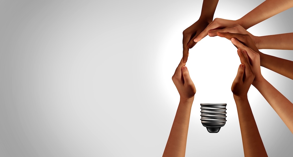 A group of hands create the outline of a lightbulb, signifying teamwork leading to creative ideas.