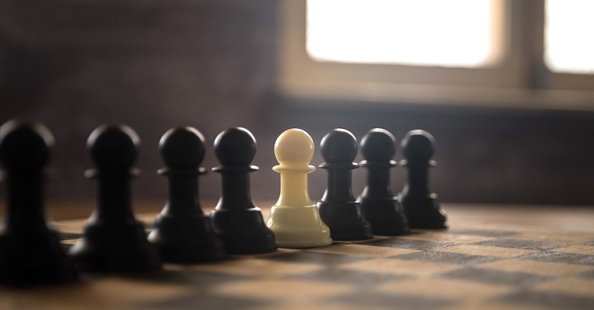 On a chess board, a white pawn stands among black pawns.