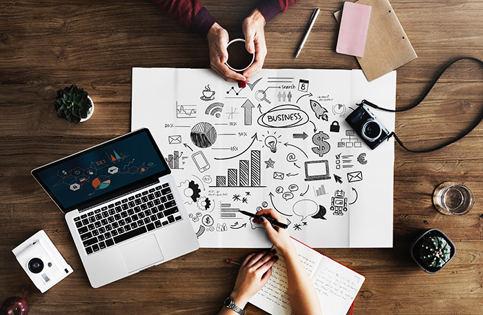 Overhead photo of the hands of two people sitting across a table drawing business related symbols