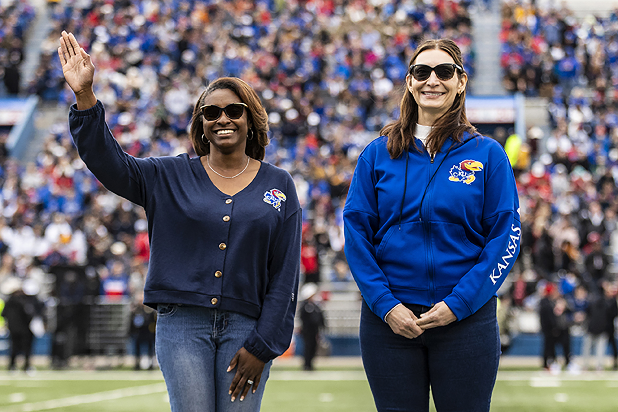 "Jomella Watson-Thompson waves to a crowd seated in a sports stadium while standing next to a another woman on the field"