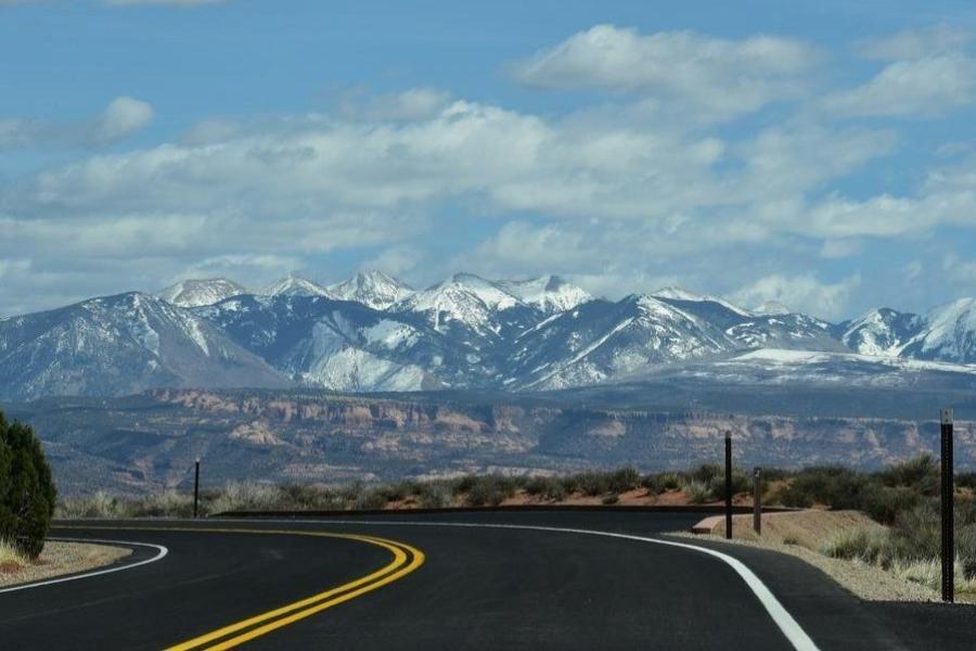 View of a winding road leading towards the snow-capped mountains under a clear blue sky.