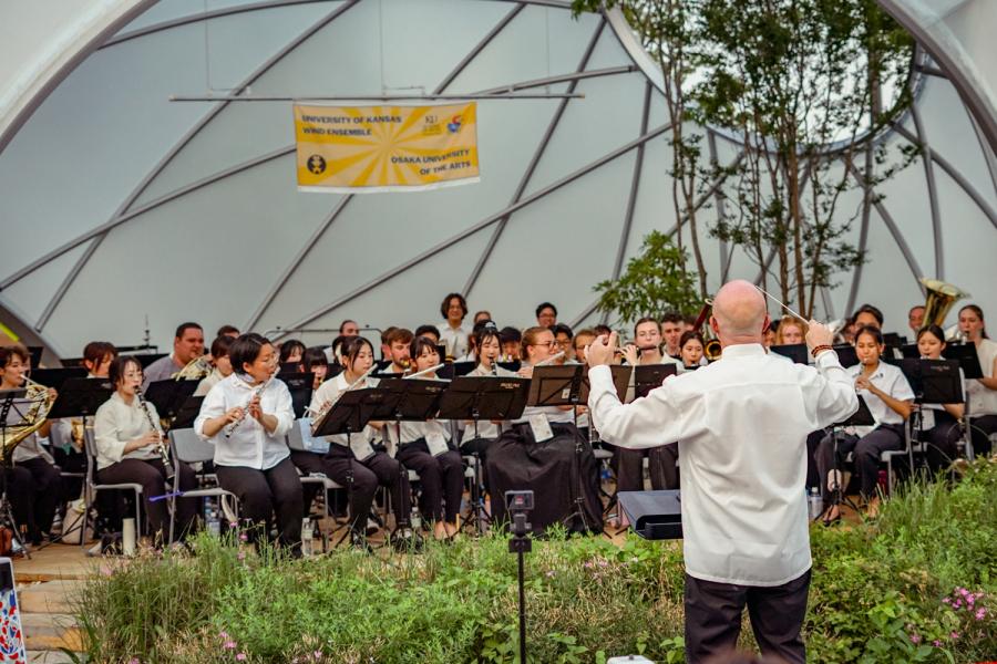 A conductor stands in front of a group of students