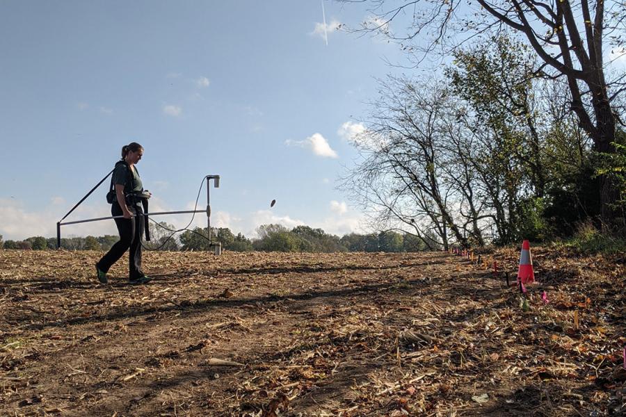 Blair Schneider carries scientific equipment through a field to collect data.