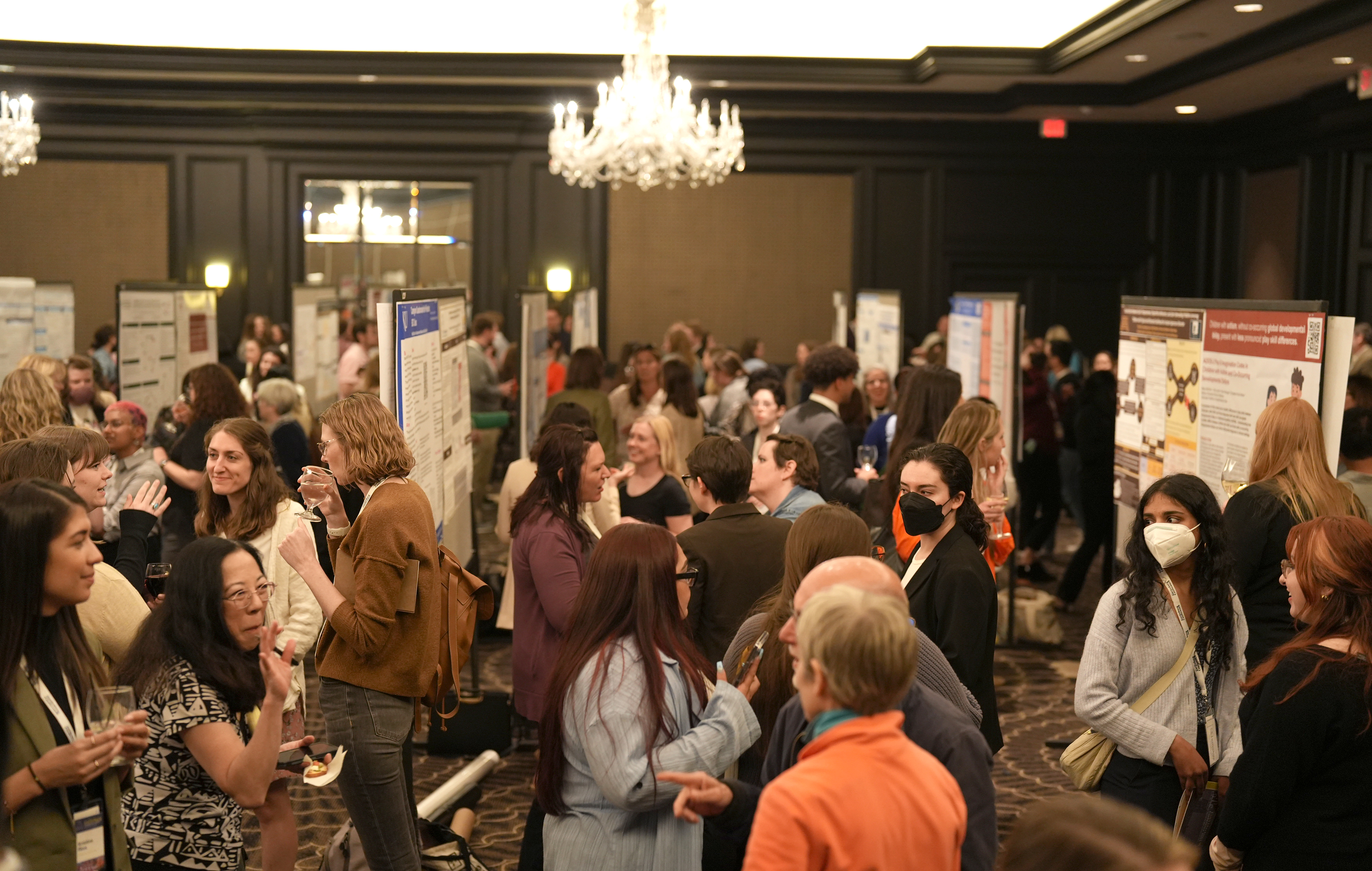 "A large crowd mingles in a ballroom during a large poster presentation"