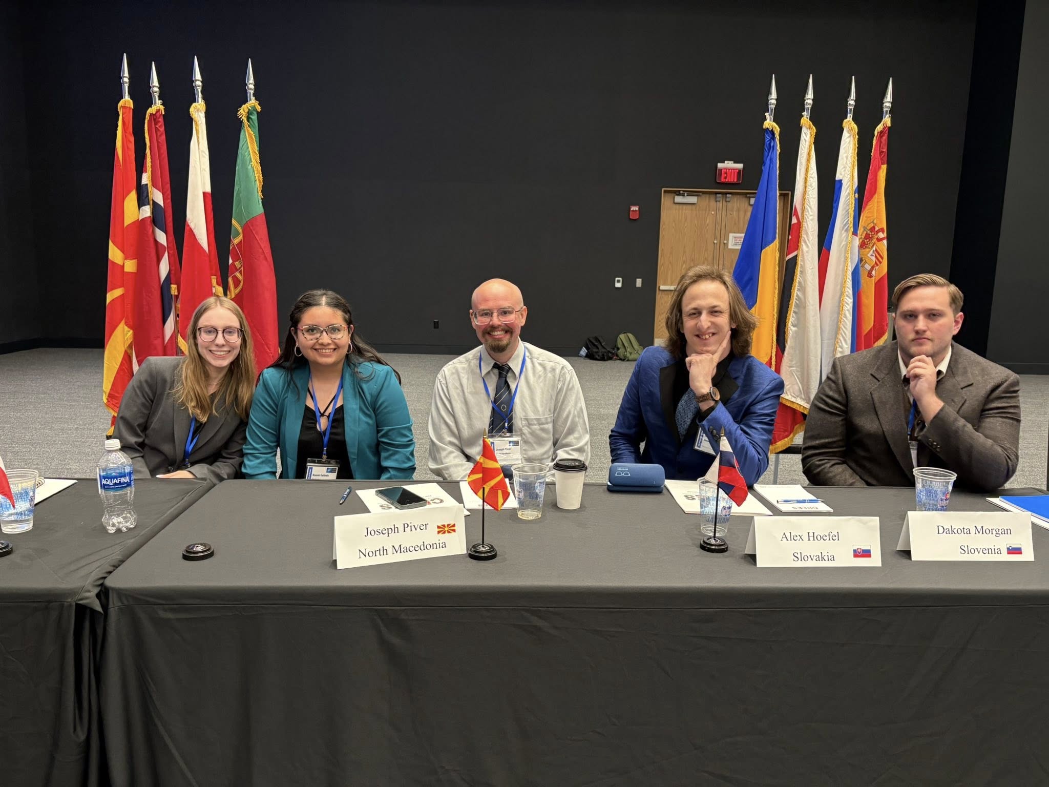 five students sitting behind a table with NATO country flags behind them
