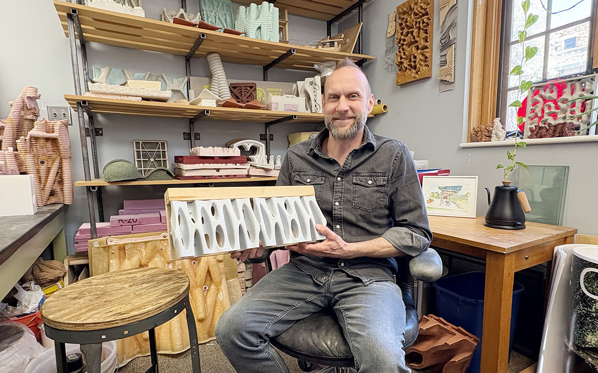 Keith Van de Riet, seated, holding a panel made to look like shoreline plant roots.