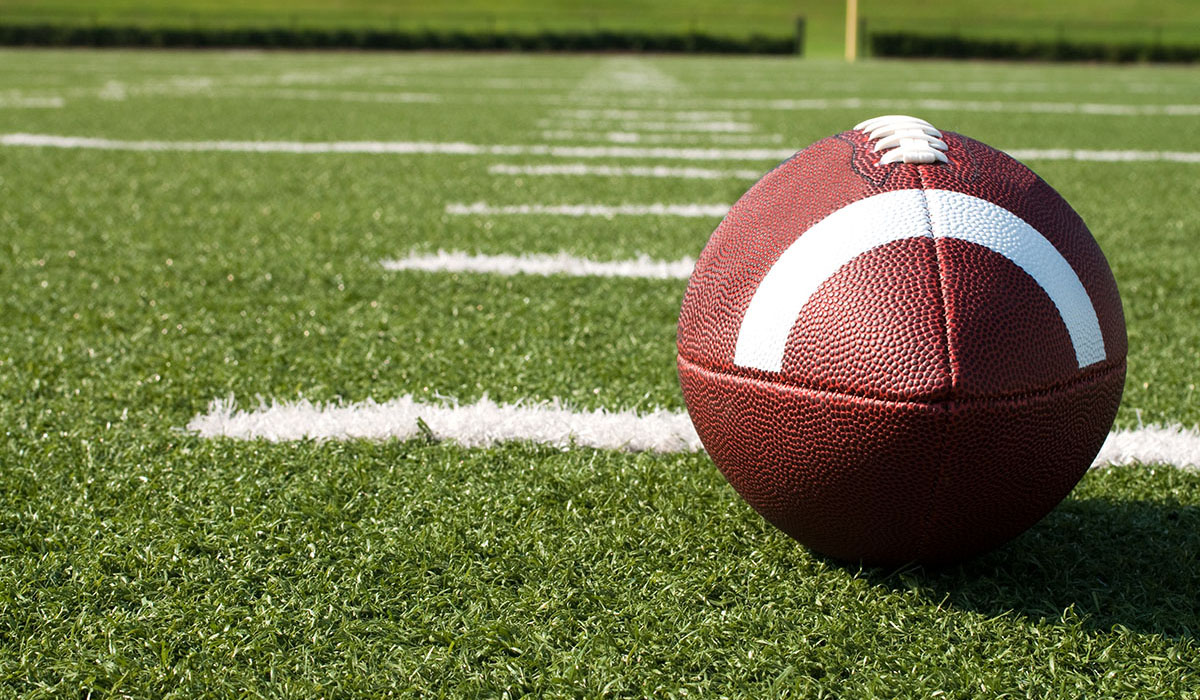 An image of a football on a field among yard markers.