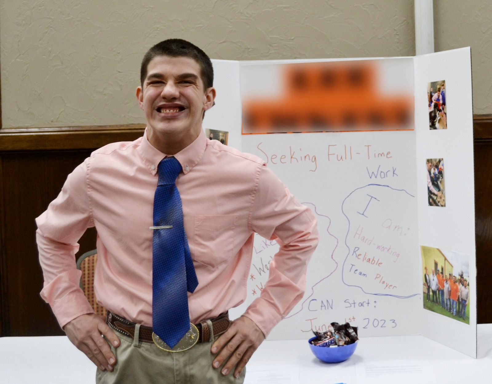 A young man wearing a blue tie and a salmon colored shirt smiles with his hands on his hips at a reverse job fair