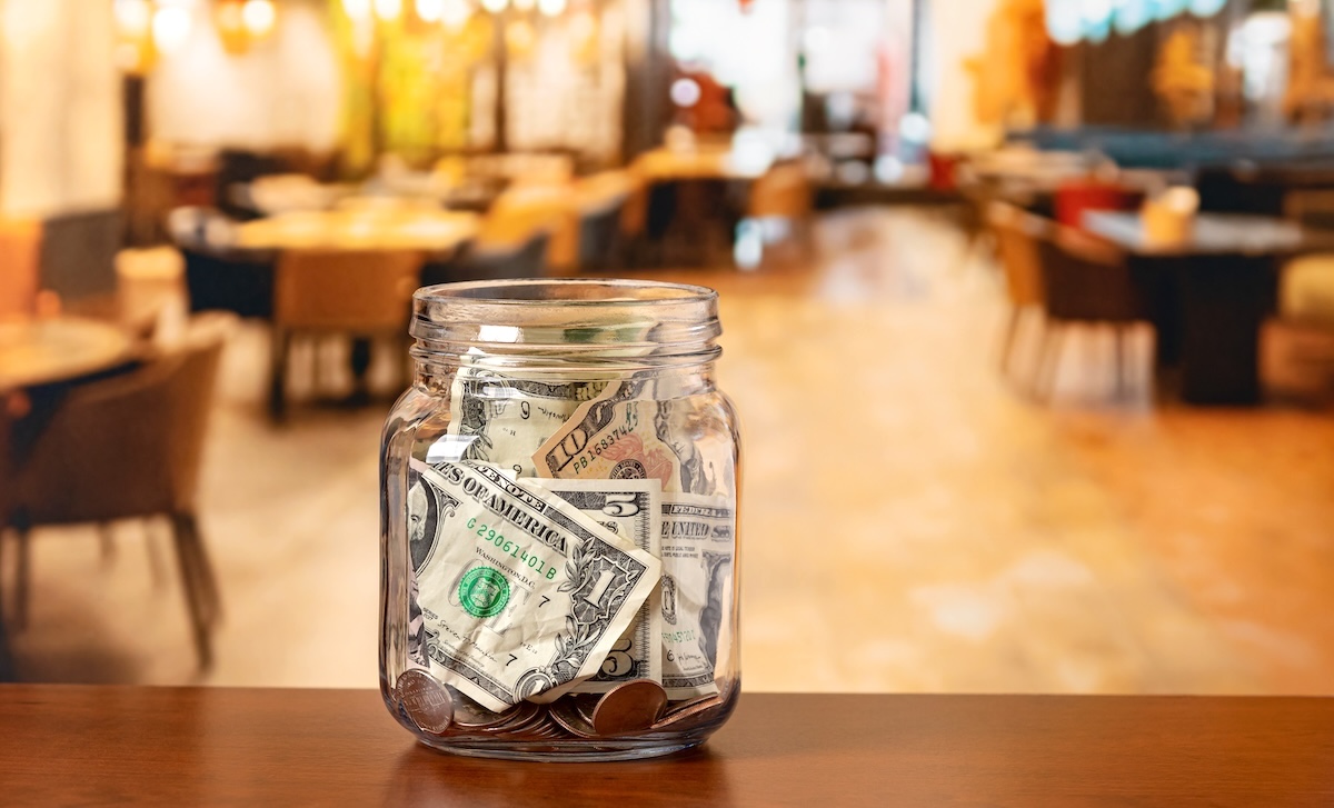 A Mason jar filled with tips sits on a counter of a restaurant.
