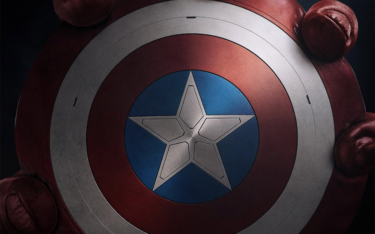 A closeup image of the shield of comic book character Captain America, held around the edges by red colored fingers of a large hand.