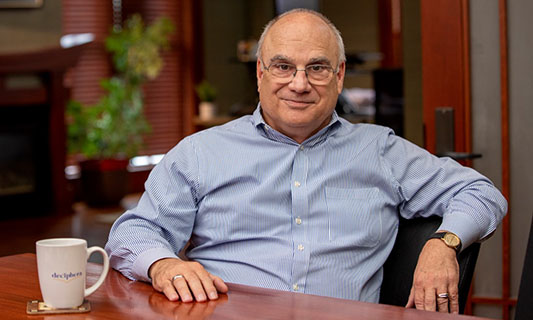 Dan Flynn, KU alumnus in pharmacy and medicinal chemistry, pictured seated in office with coffee mug with Deciphera logo.