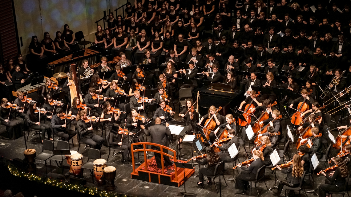 A symphony performing onstage with a large choir behind them