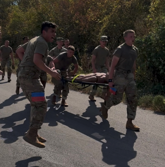 Cadet Ben Gomez roots on teammates Nate Lundgren, Olathe, and Hayden Shriver, Topeka, as they carry a stretcher.