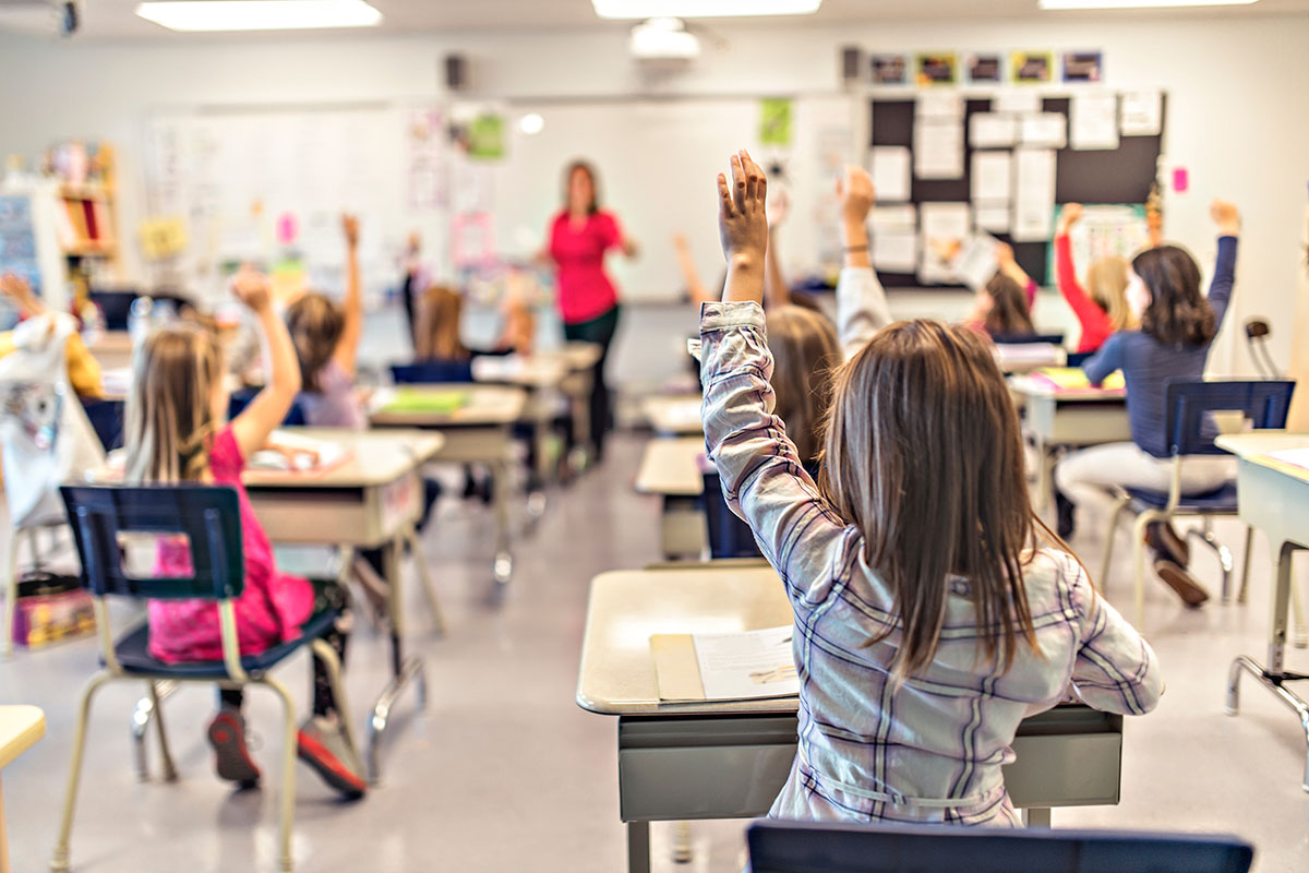 An image of young students in a classroom with one student raising her hand.