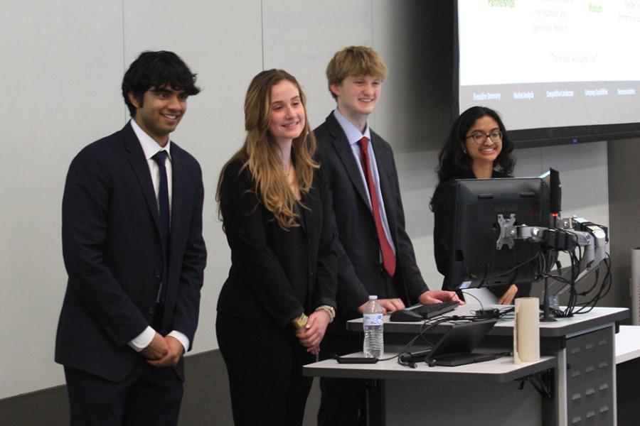 A team of four students standing at a lectern presenting to a panel of judges in a classroom in Capitol Federal Hall.