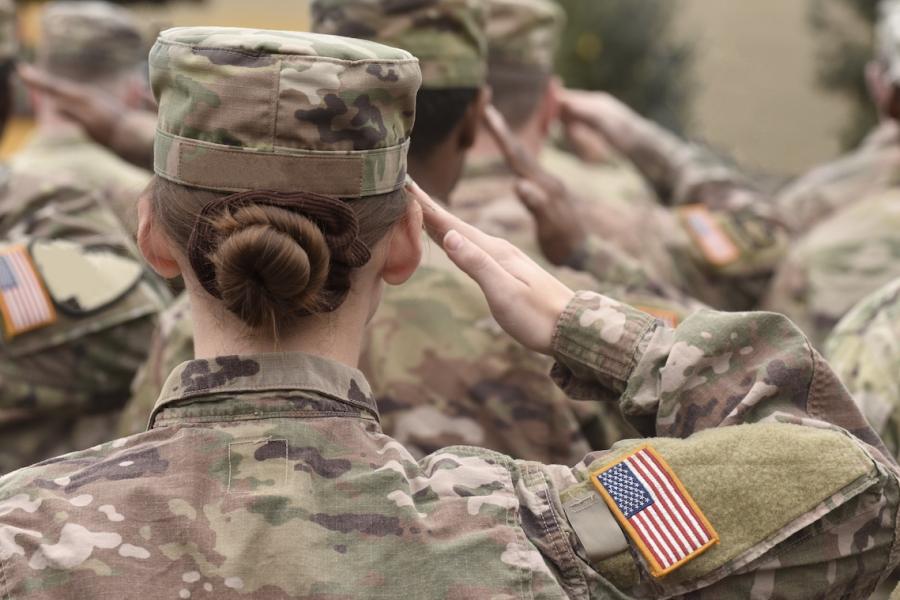 An American woman soldier stands in formation with fellow soldiers while saluting.