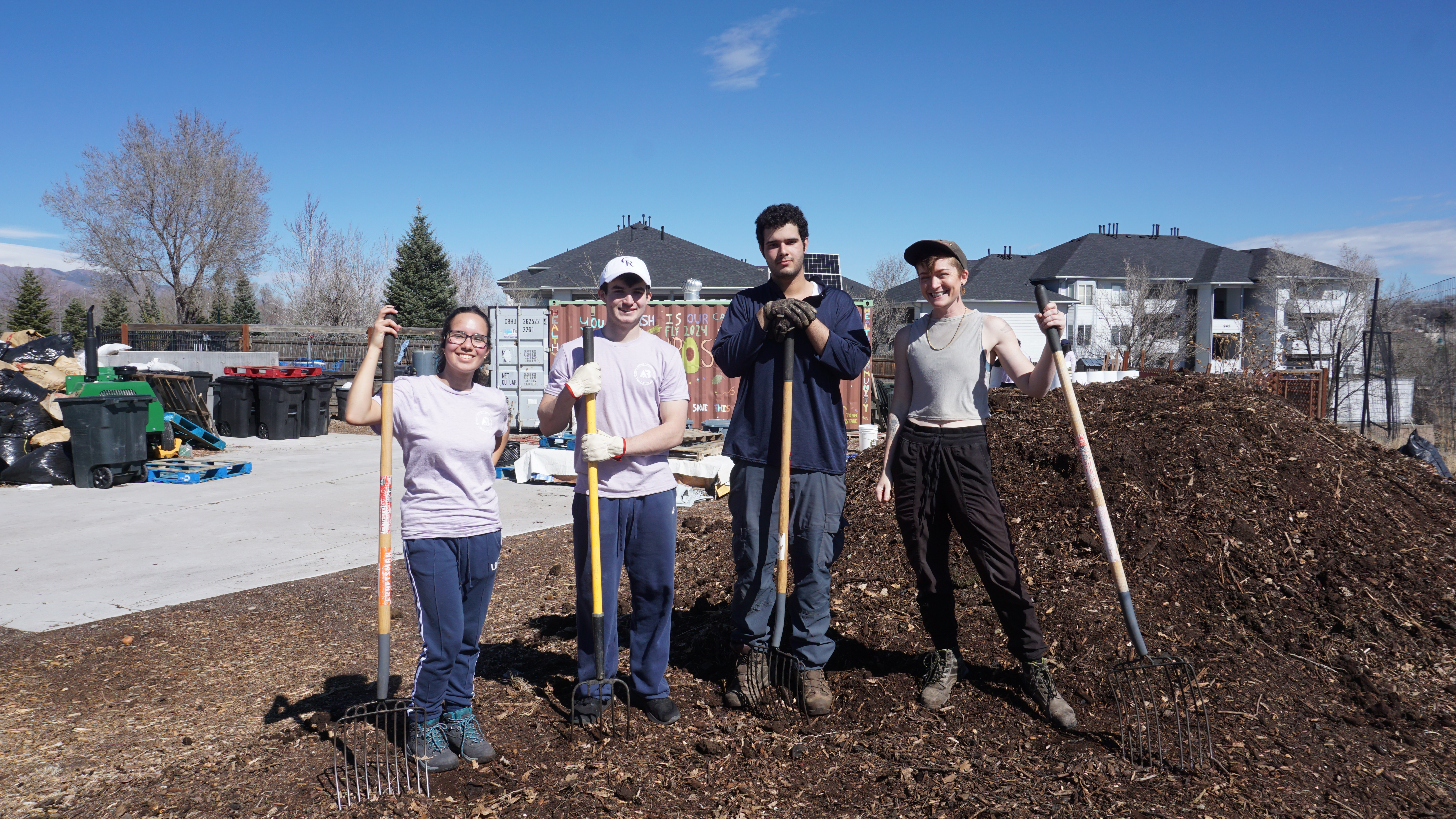 Students stand with gardening hoes outside outdoor project space.