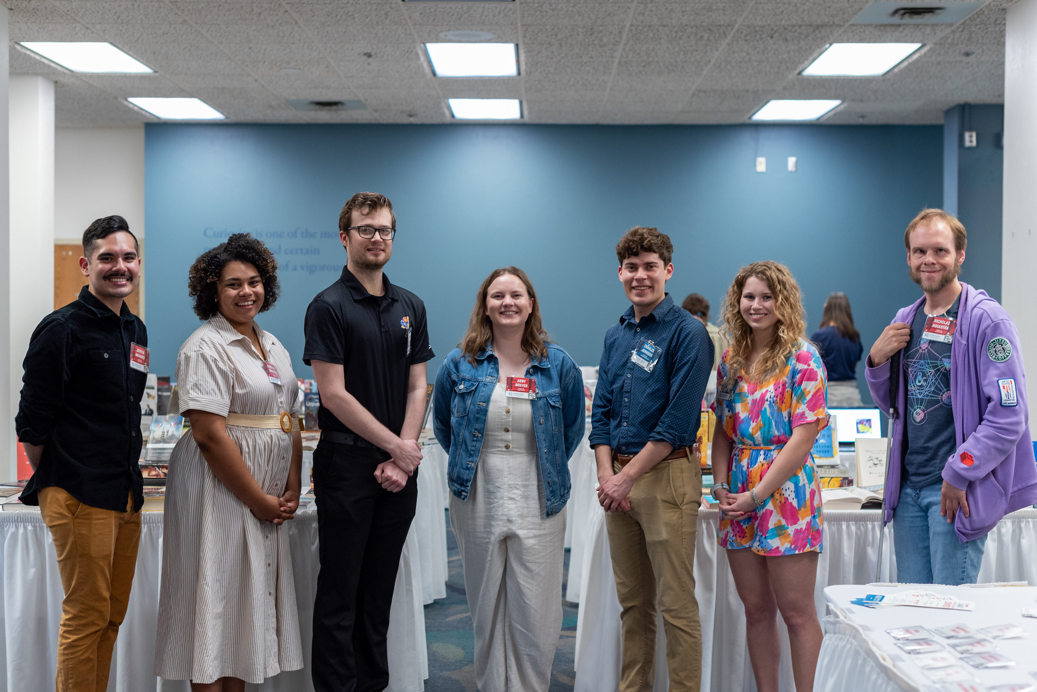 Seven contestants in the Snyder Book Collecting Contest pose in a line in the midst of tables displaying book collections.