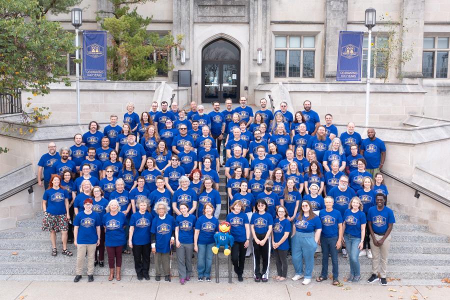 KU Libraries faculty and staff gather on the front steps of Watson Library wearing centennial celebration t-shirts.