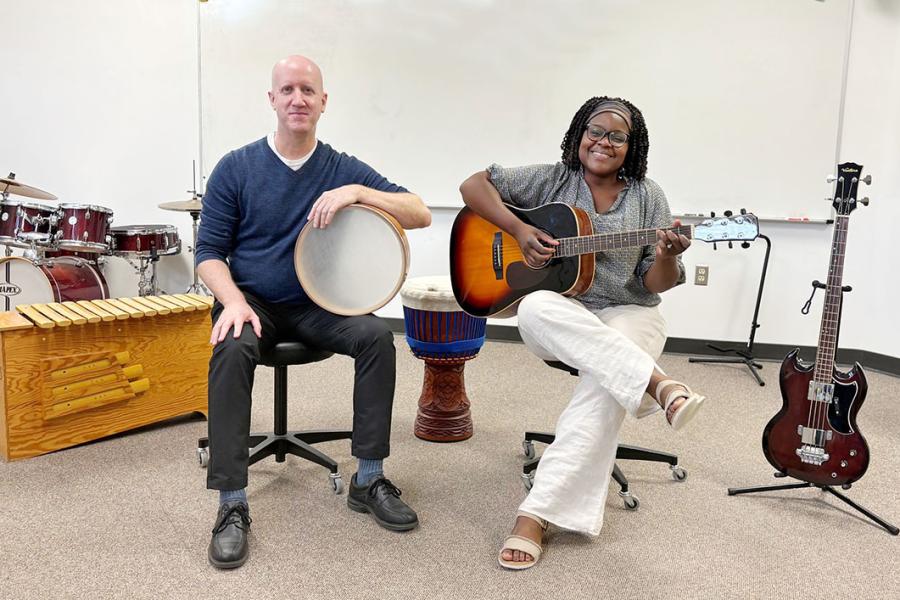 Man, seated, holding drum. Woman, seated, holding guitar. Other instruments around.