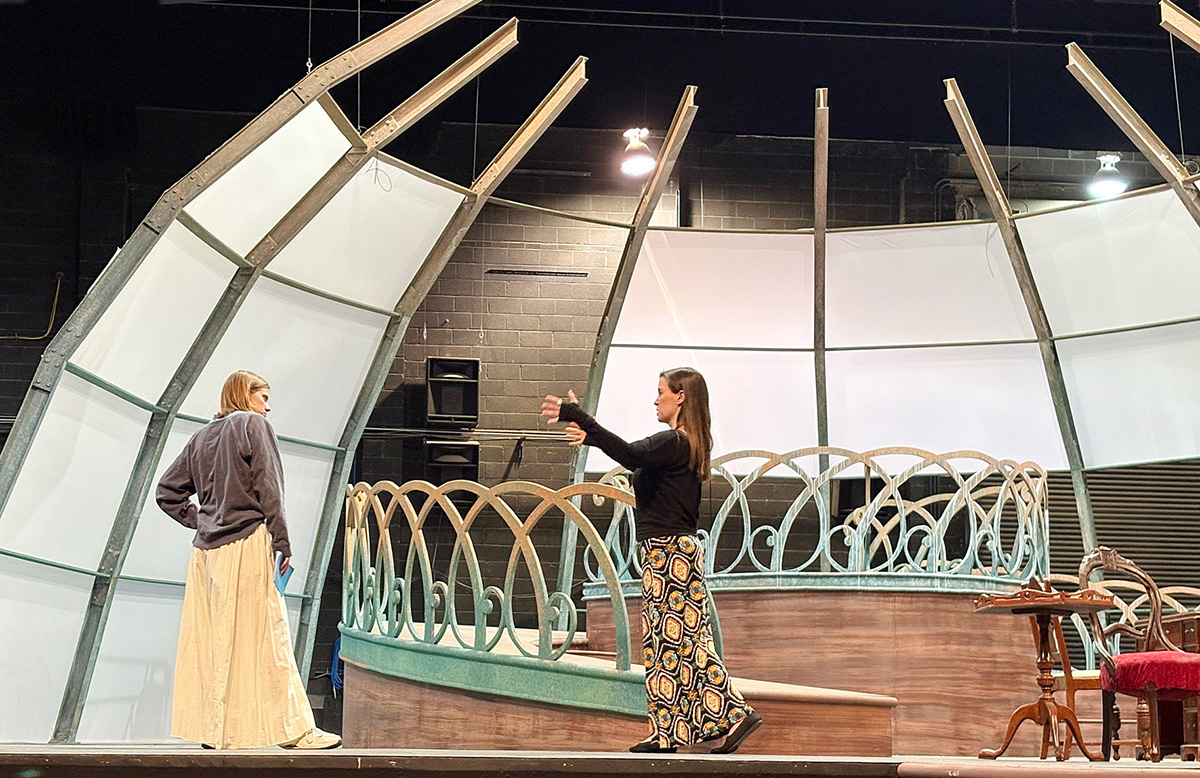 Two women standing on University of Kansas stage, one with script in hand.
