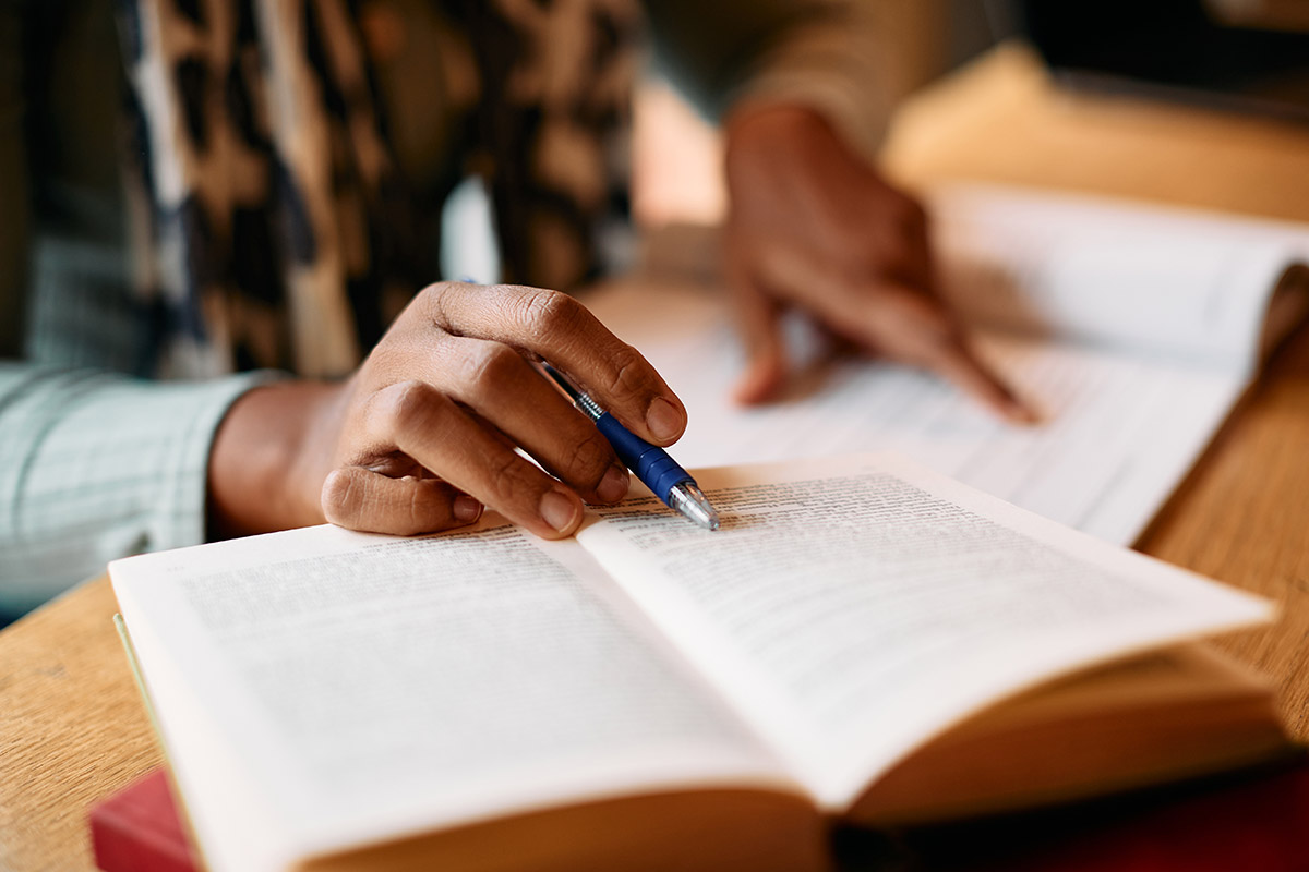 A close up photo of an adult woman's hands holding a book and writing in a notebook.