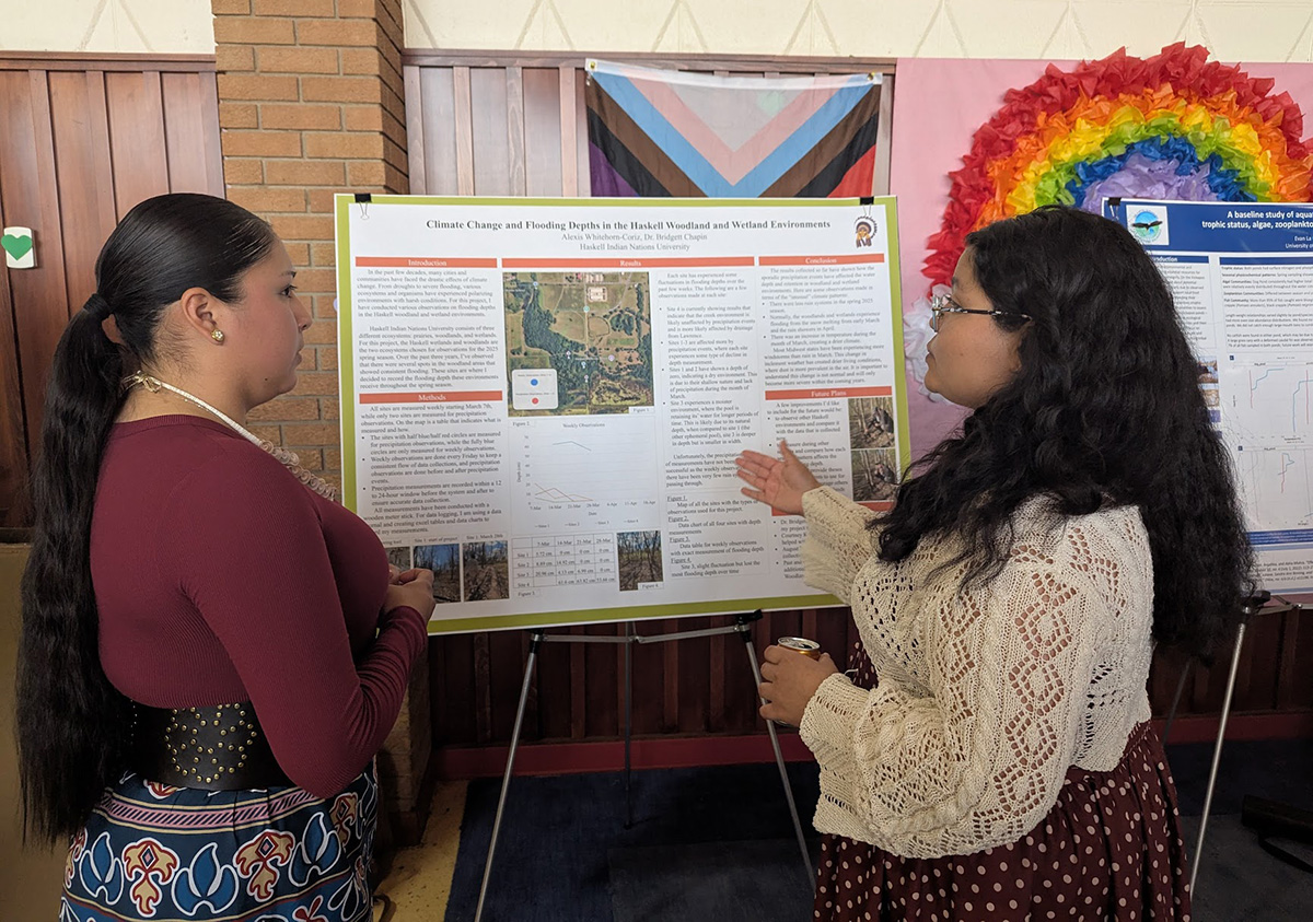 A presenter and audience member confer over a research poster at the 2025 KU-Haskell Research Symposium.