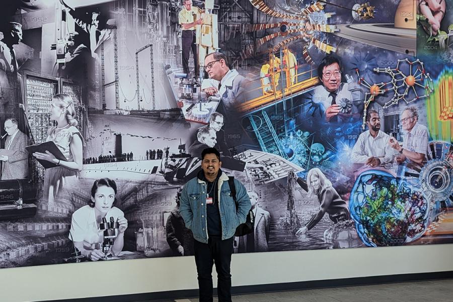 An image of KU graduate student Amrit Gautam standing in front of a mural at the Oak Ridge National Laboratory in Tennessee.