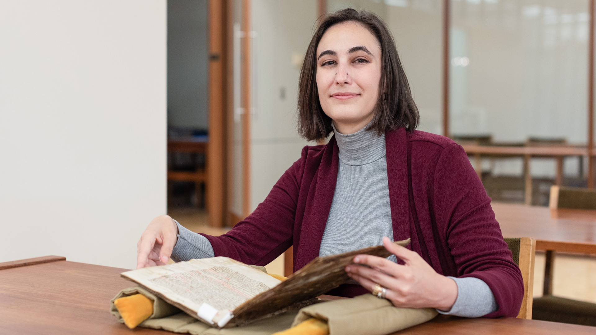 Eve Wolynes poses with an item in the Spencer Research Library Reading Room