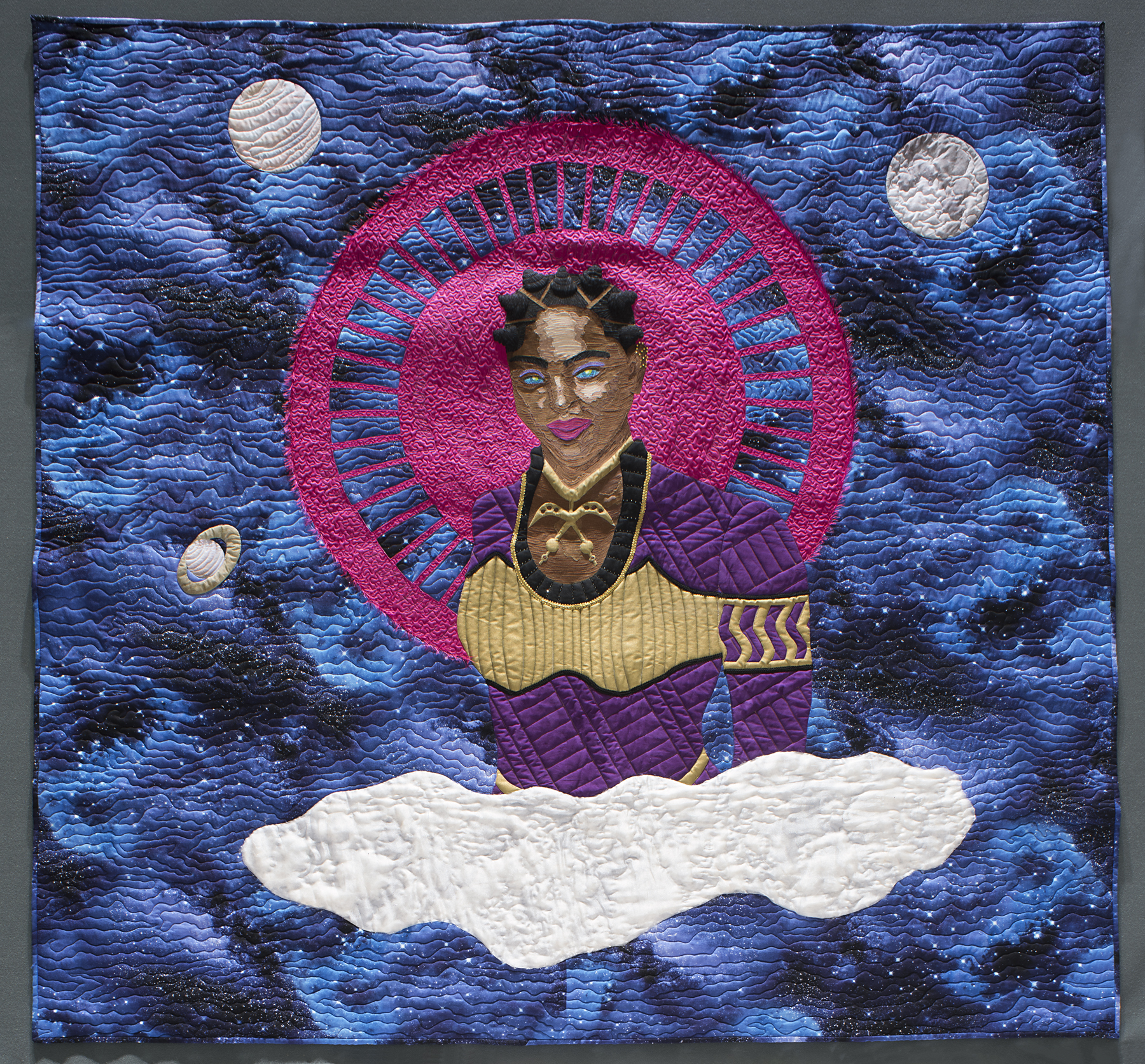 A square quilt with a blue, celestial background and a Black woman wearing purple and gold with a pink halo in the center