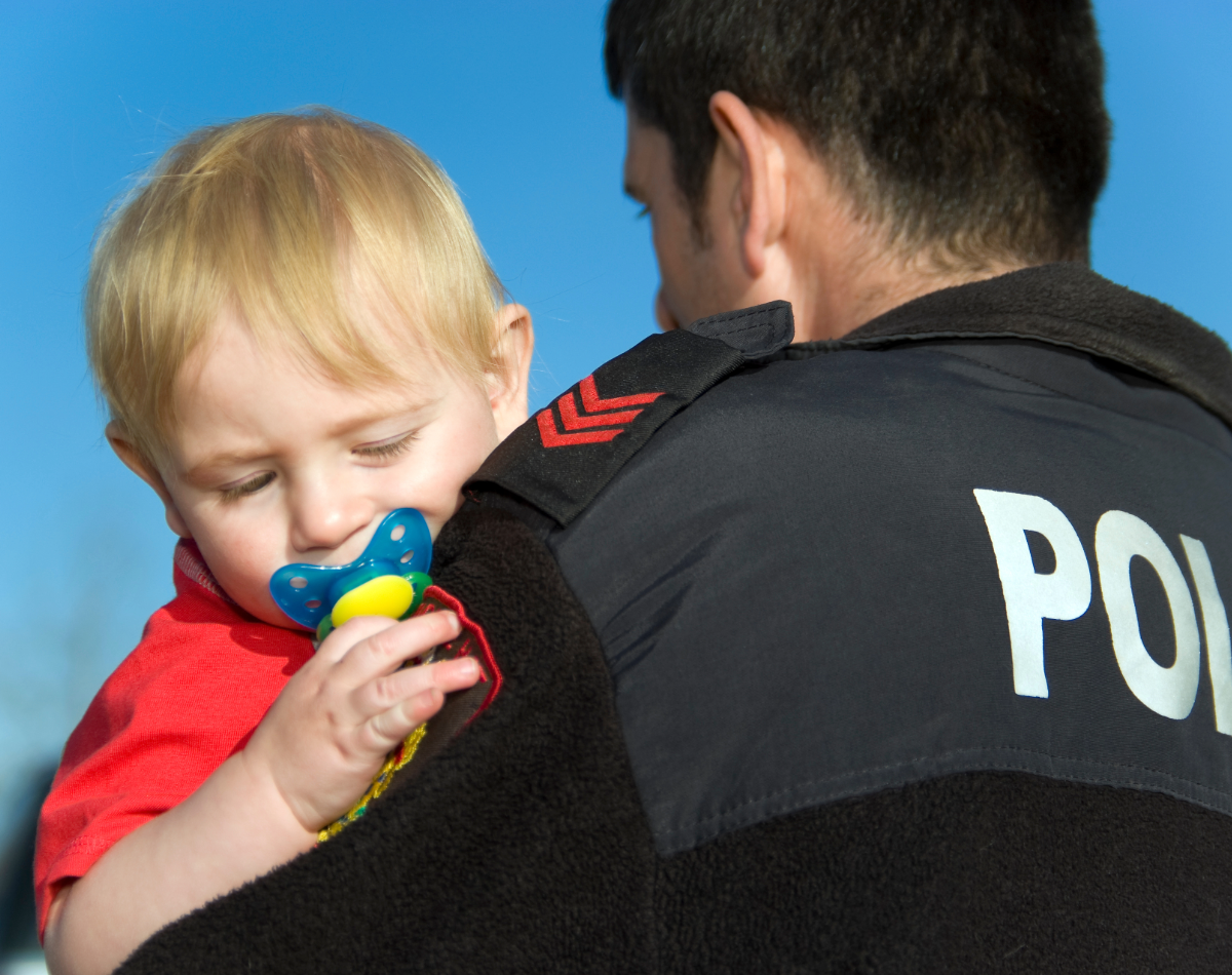 A police officer holds a toddler who is sucking a pacifier