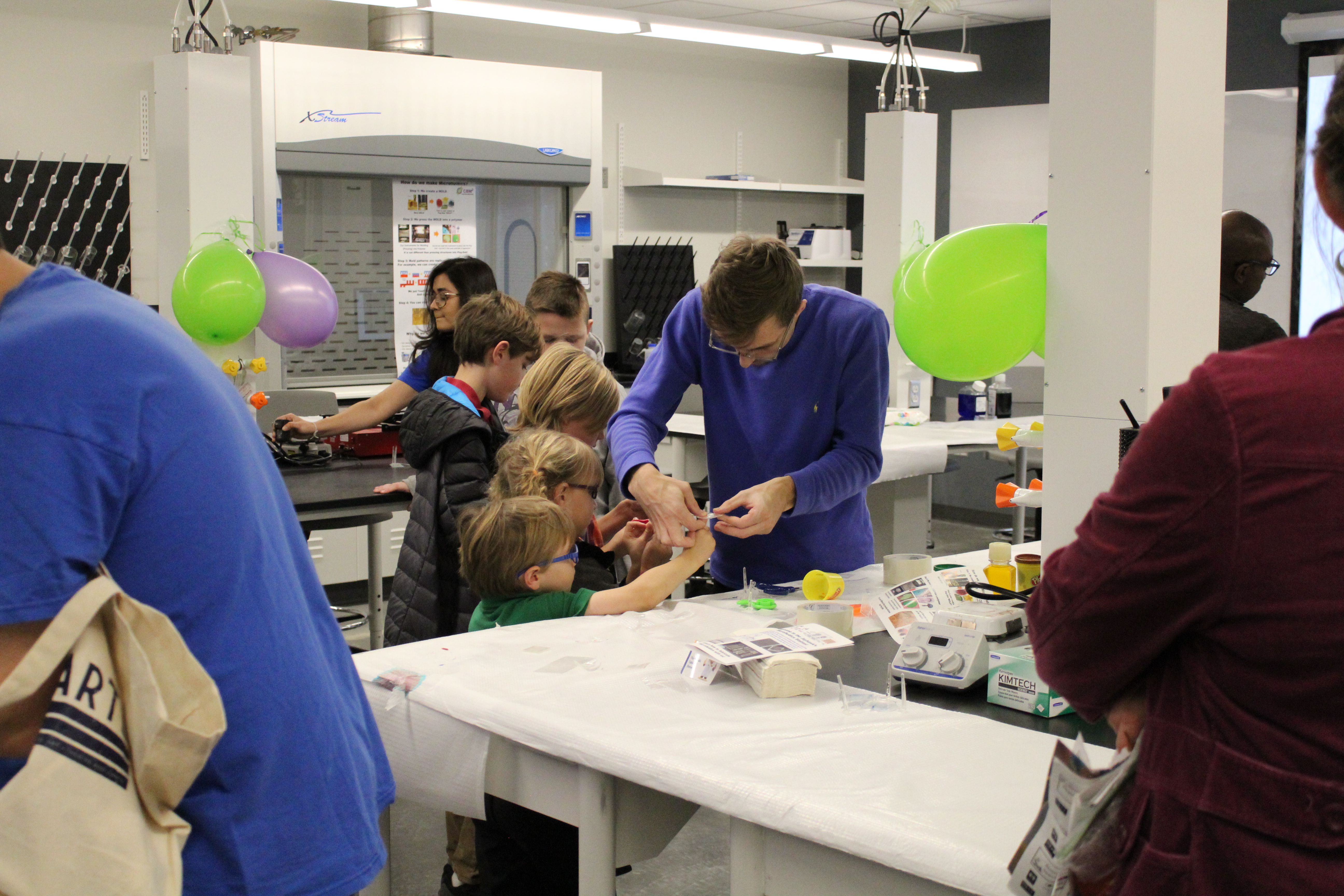 An adult helper assisting two children with modeling clay (Play-Doh).