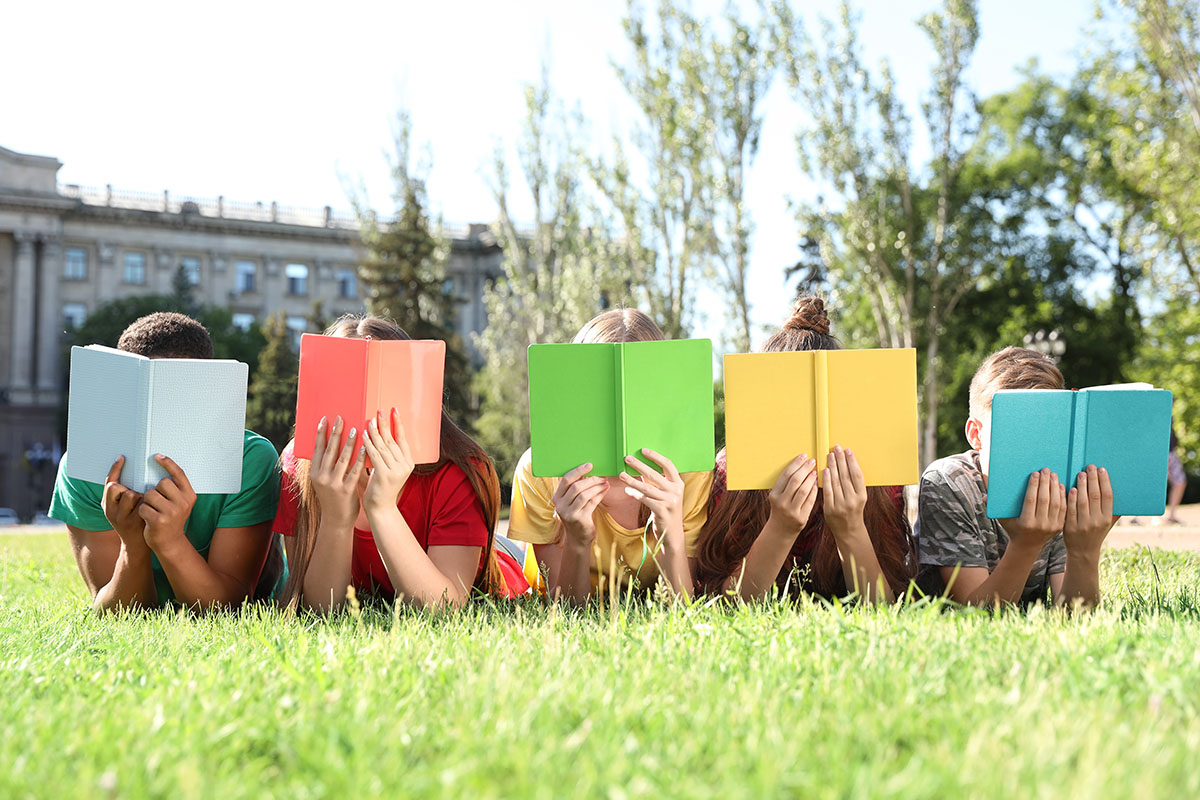 An image of several children lying on a grassy lawn reading books.