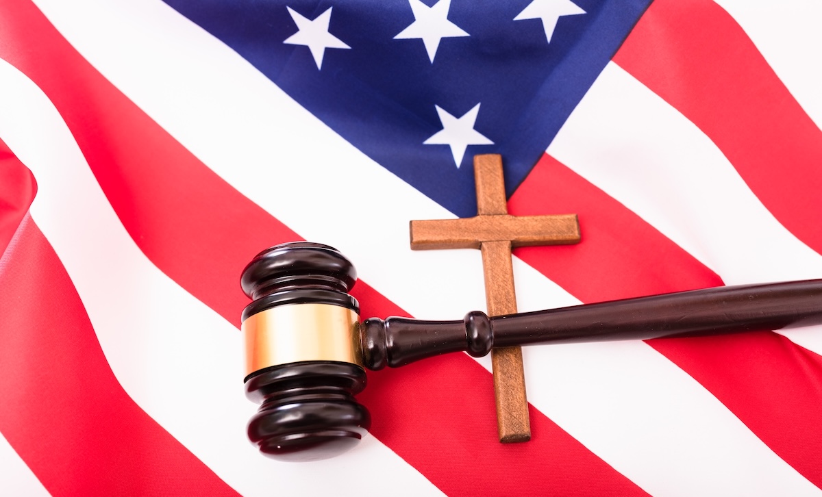 A gavel sit on top of a cross, which sit upon an American flag.