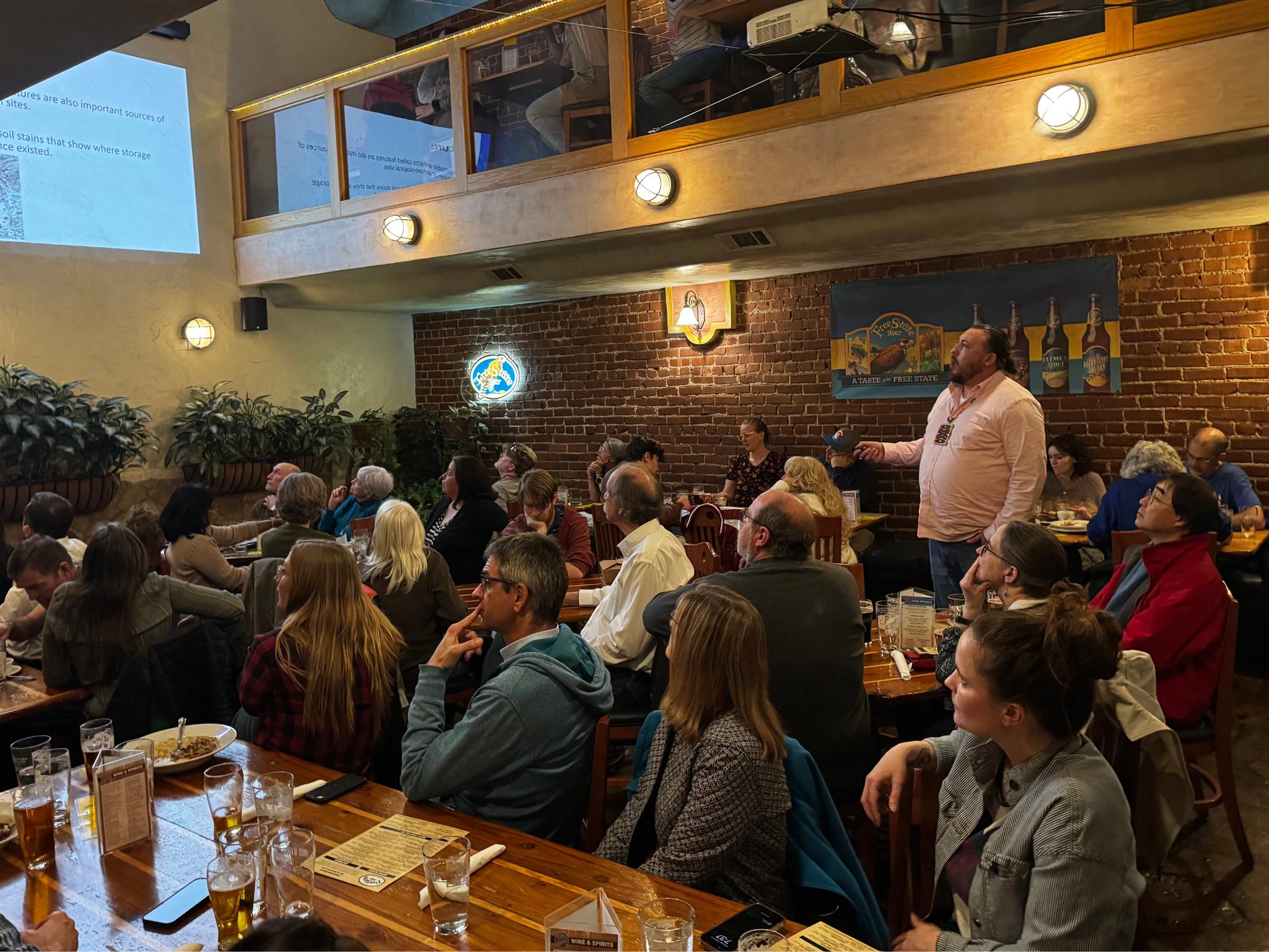 Carlton stands in Free State Brewing Company's beer hall, addressing a room full of people on artifacts from the Great Plains.