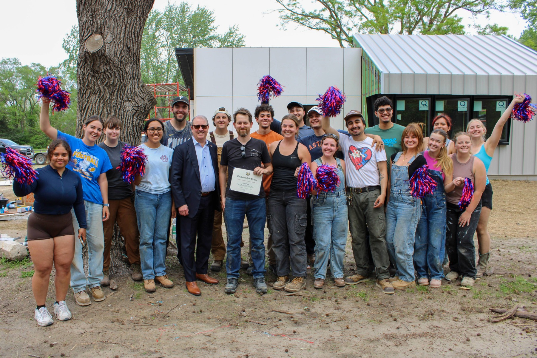 Professor Chad Kraus poses with Kemper fellowship certificate alongside Chancellor Girod and class in front of construction project