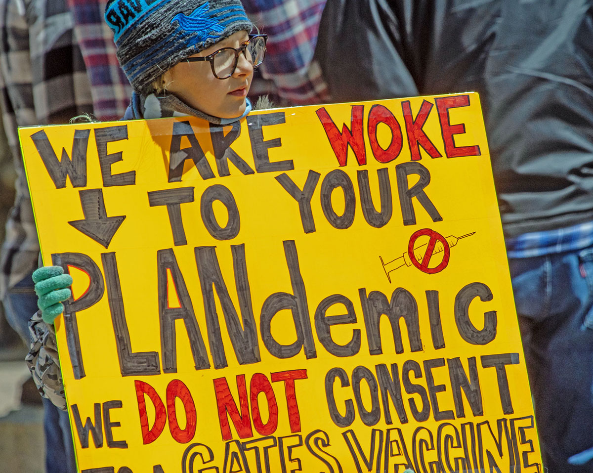 Young protester holds sign referring to the so-called plan-demic.