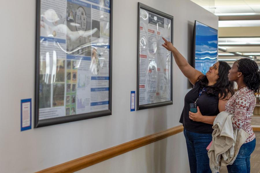 Two visitors look at a row of research posters on the wall of Anschutz Library.