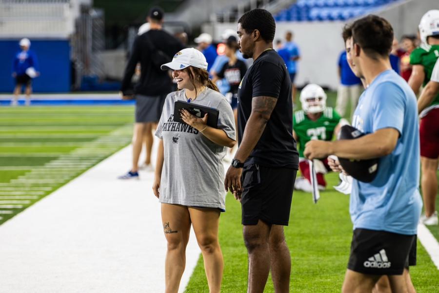 KU football players and JAPL graduate research assistance Madi Rink on a football field holding an iPad.