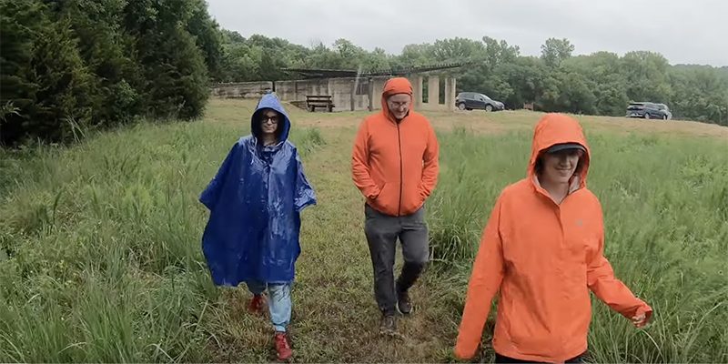 Three people in brightly colors raincoats walking in field