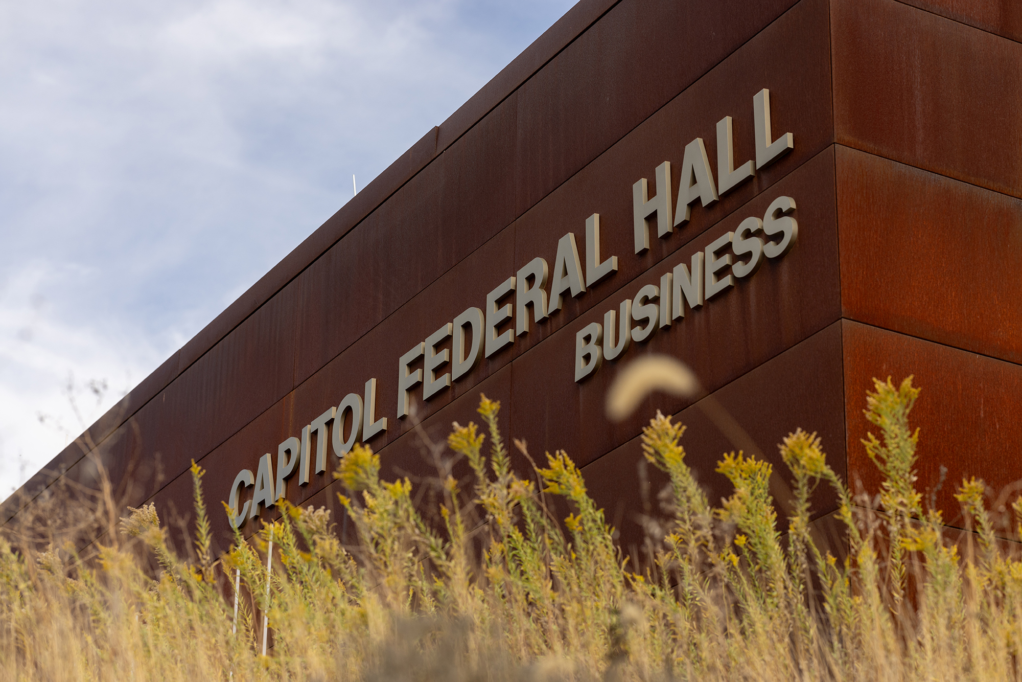 Detail photo of "Capitol Federal Hall, Business" text on the exterior of the building with tallgrass in the foreground