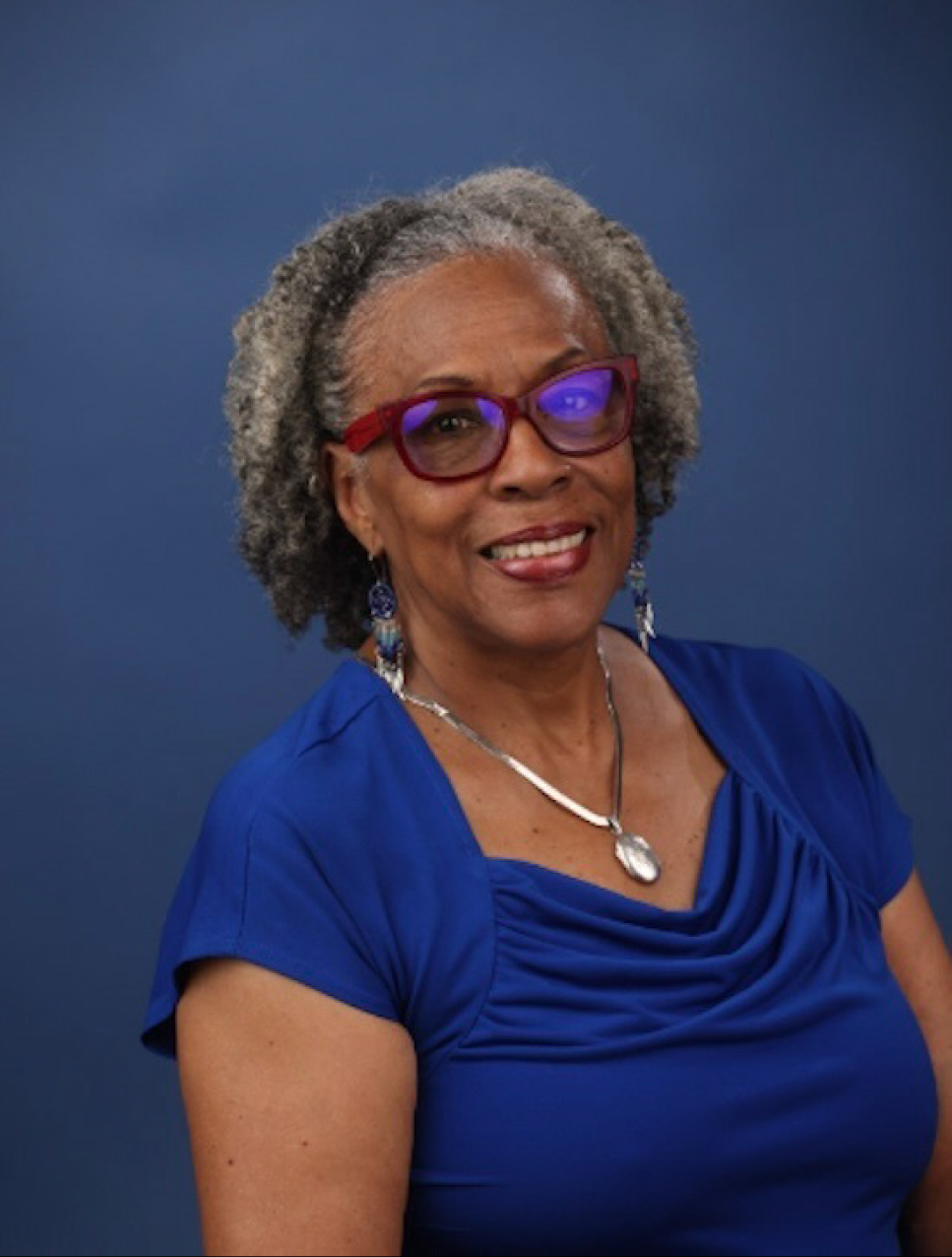 Maryemma Graham smiles in a portrait photo wearing a blue shirt and red glasses