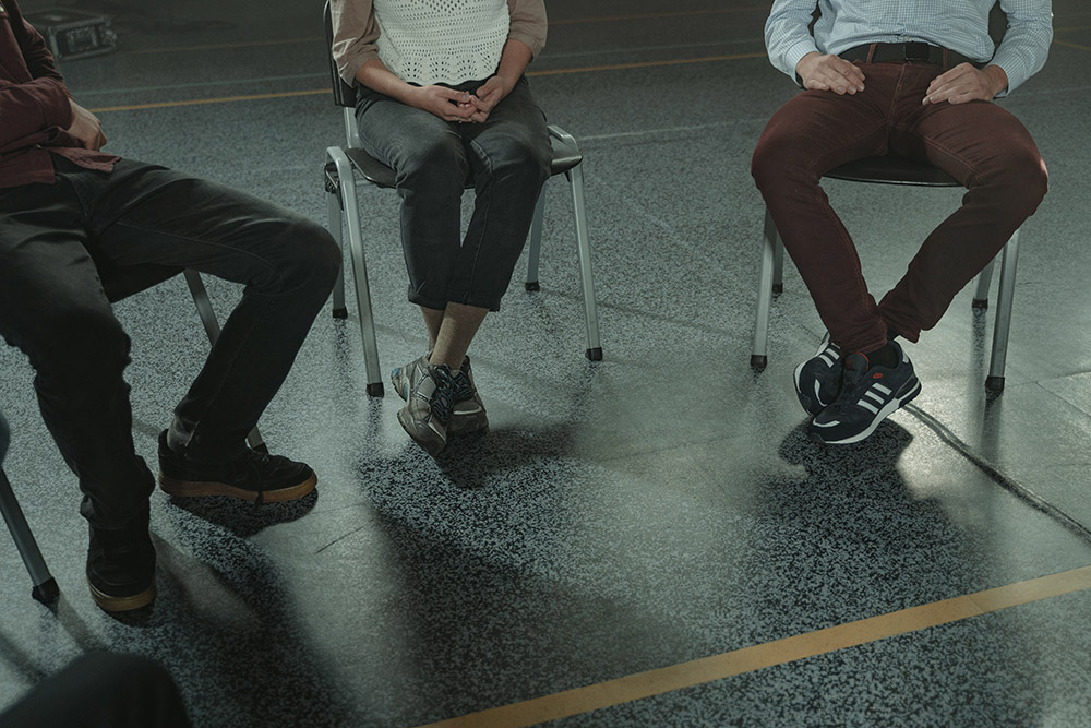 View from chest down of individuals sitting in circle during support group meeting. Pexels image.